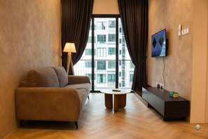 A modern living room with a sofa, a lamp, a coffee table, a TV, and a view of a building through large windows.