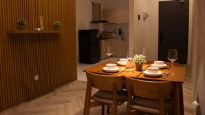 Un comedor con una mesa de madera dispuesta para cuatro personas, rodeada de sillas, y una cocina al fondo.