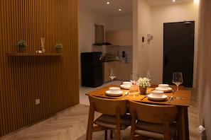 Een eetgedeelte met een tafel voor vier personen, een keuken op de achtergrond en een donkere deur aan de rechterkant.