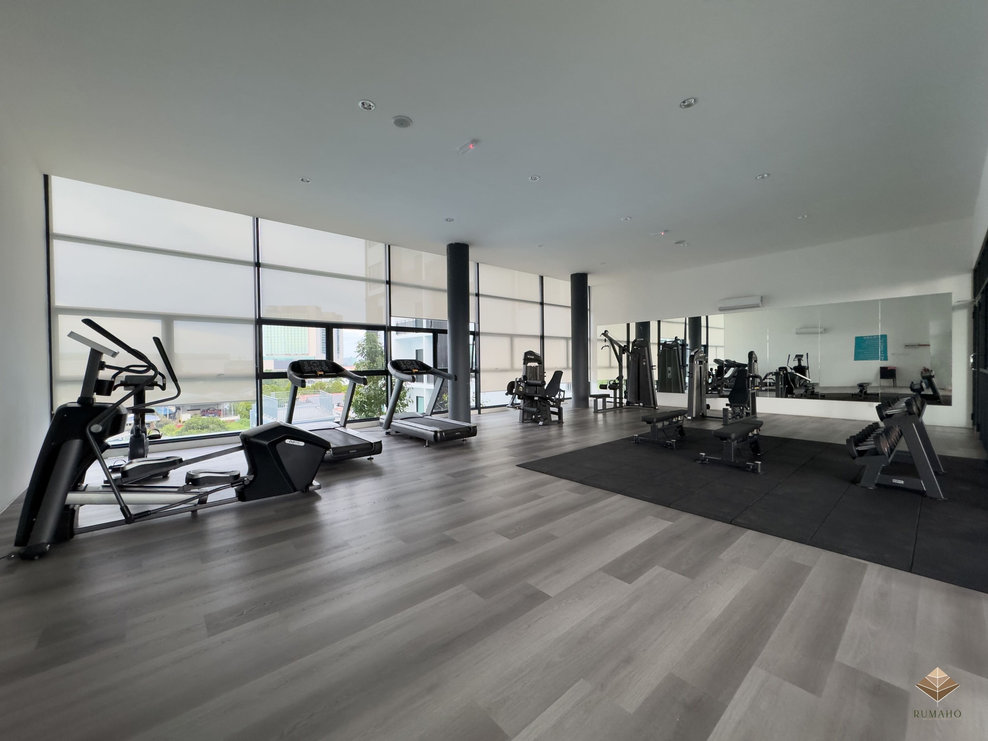 A modern gym with cardio machines, free weights, and a large window providing a view of the city.