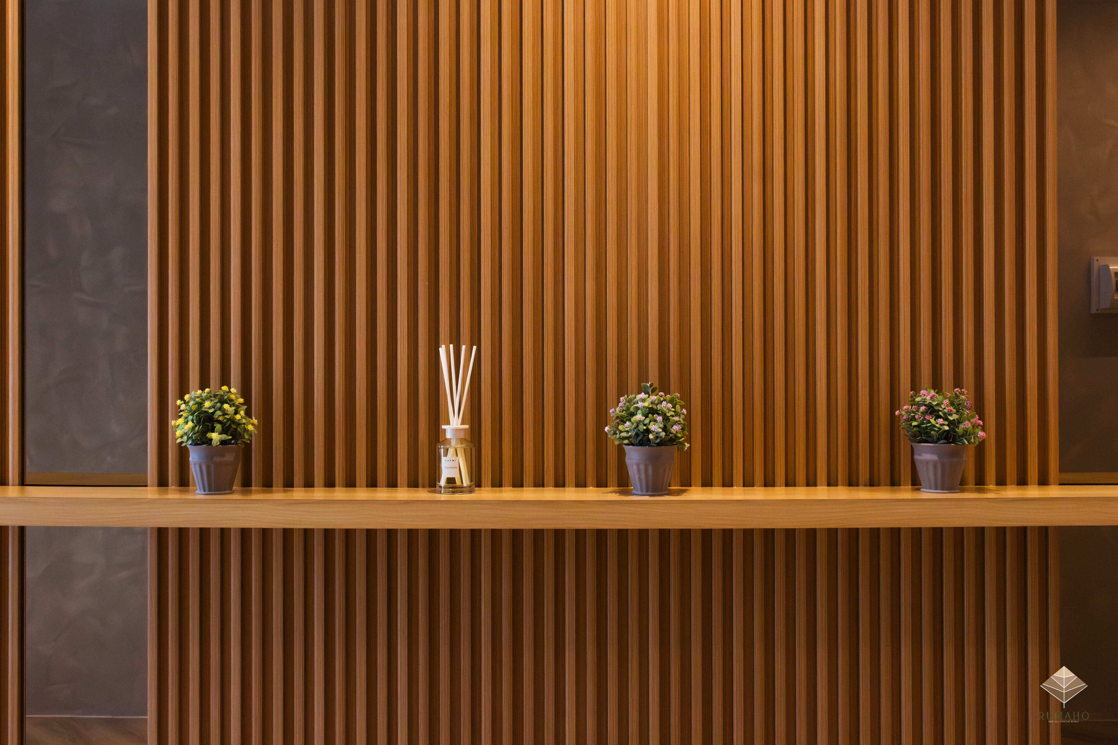 A reception desk with a wooden slat wall, potted plants, and a glass container with reed diffusers.