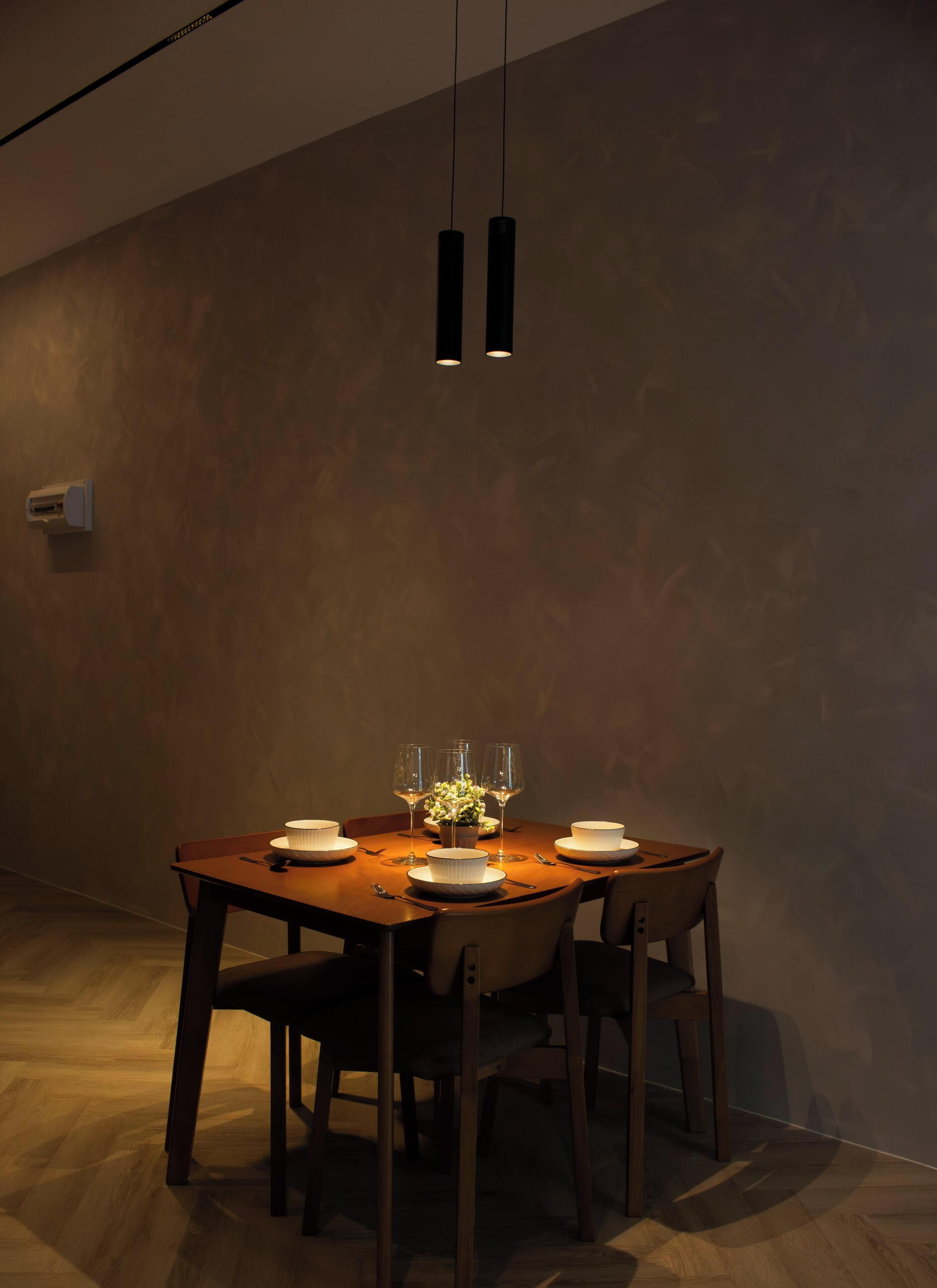 Een eetgedeelte met een houten tafel, vier stoelen, een vaas met bloemen en twee hanglampen.