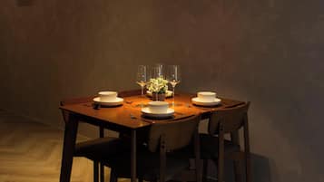 Een eetgedeelte met een houten tafel, vier stoelen, een vaas met bloemen en twee hanglampen.
