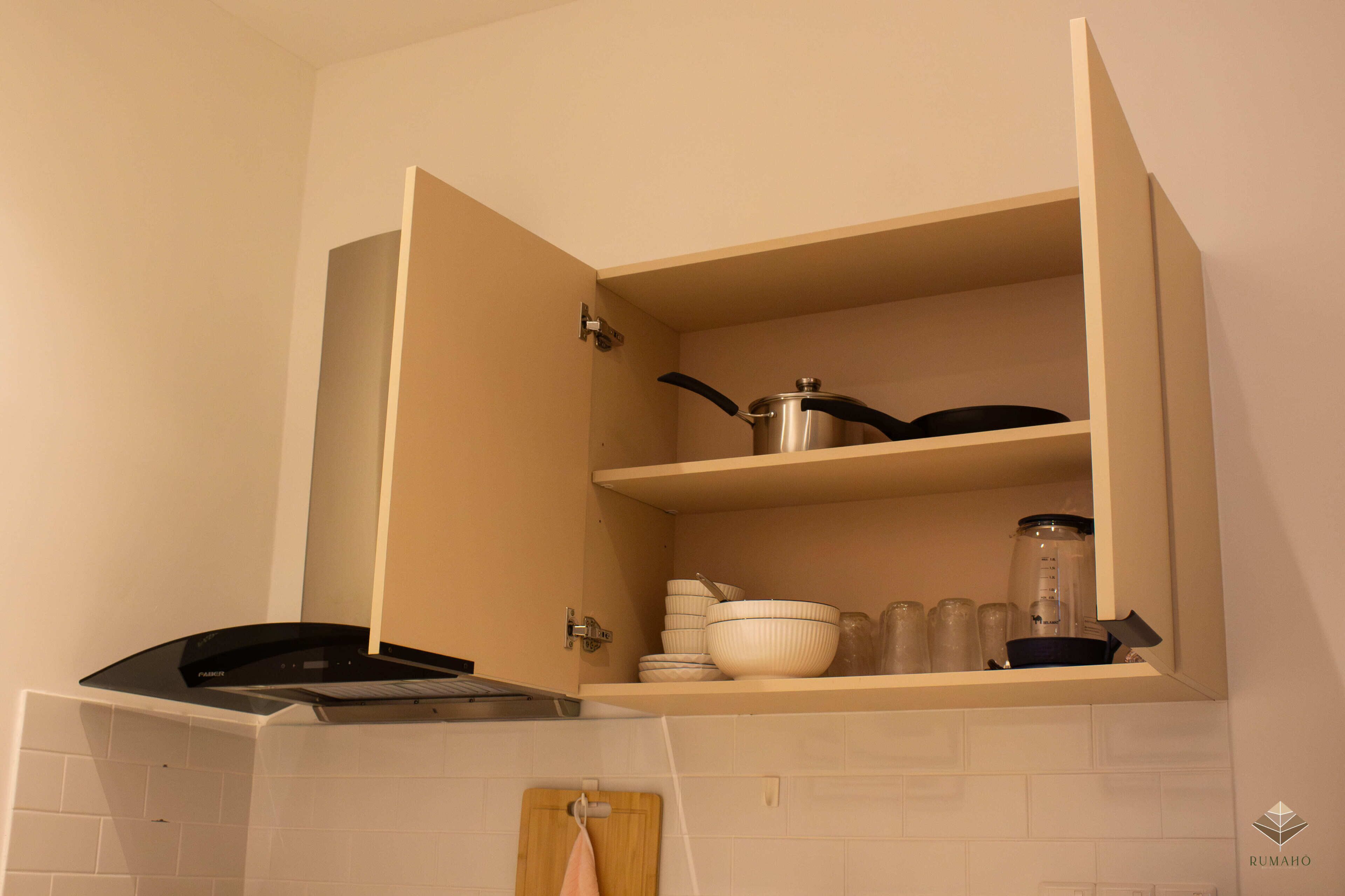 Een keuken met een ingebouwde oven, een aanrecht met een snijplank en een kast met servies en potten.