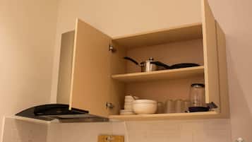 Een keuken met een ingebouwde oven, een aanrecht met een snijplank en een kast met servies en potten.