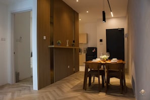 Een moderne eetruimte met een houten scheidingswand, een gedekte tafel voor twee personen en een zwart hanglamp.