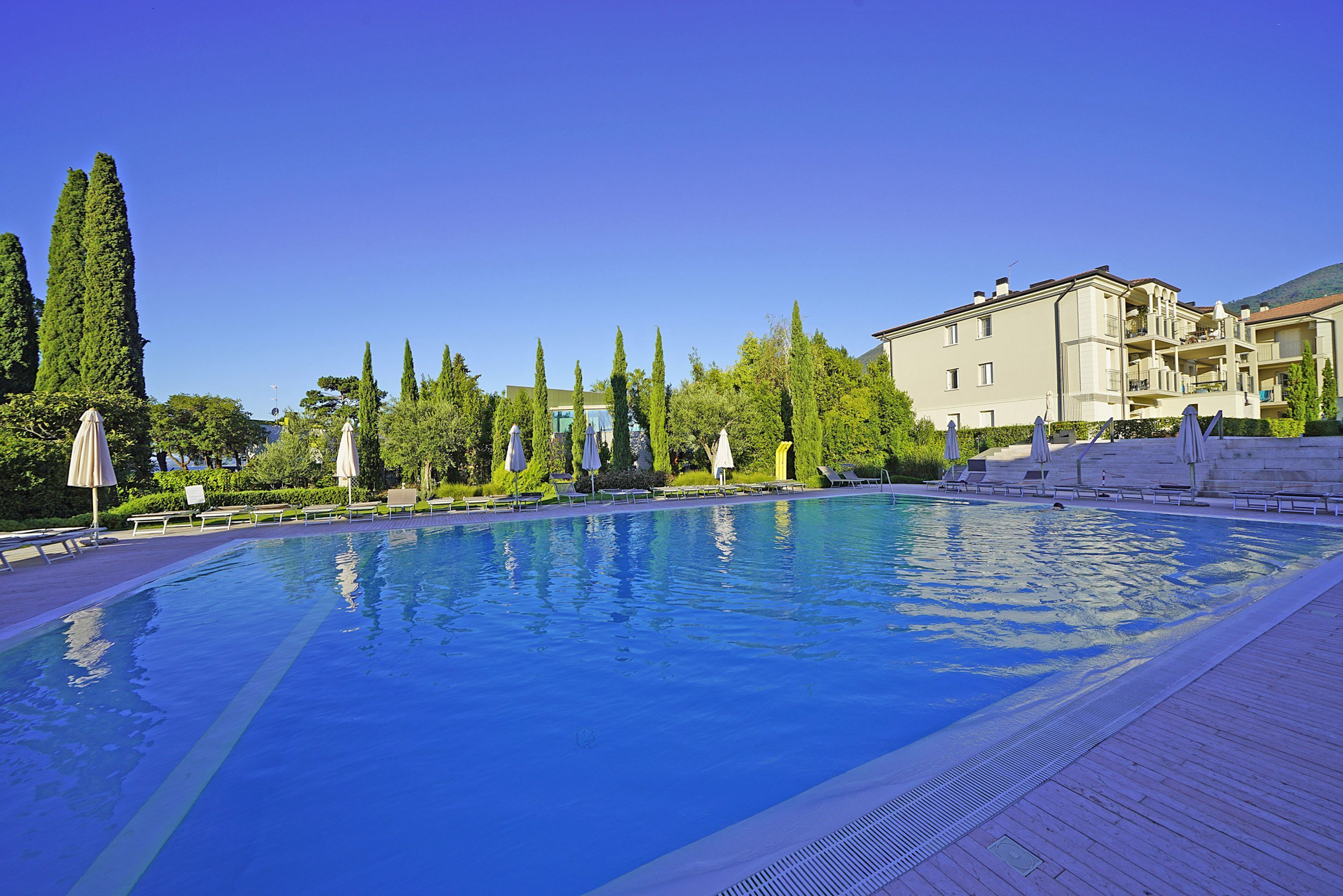A swimming pool with lounge chairs and umbrellas, surrounded by trees and a building.