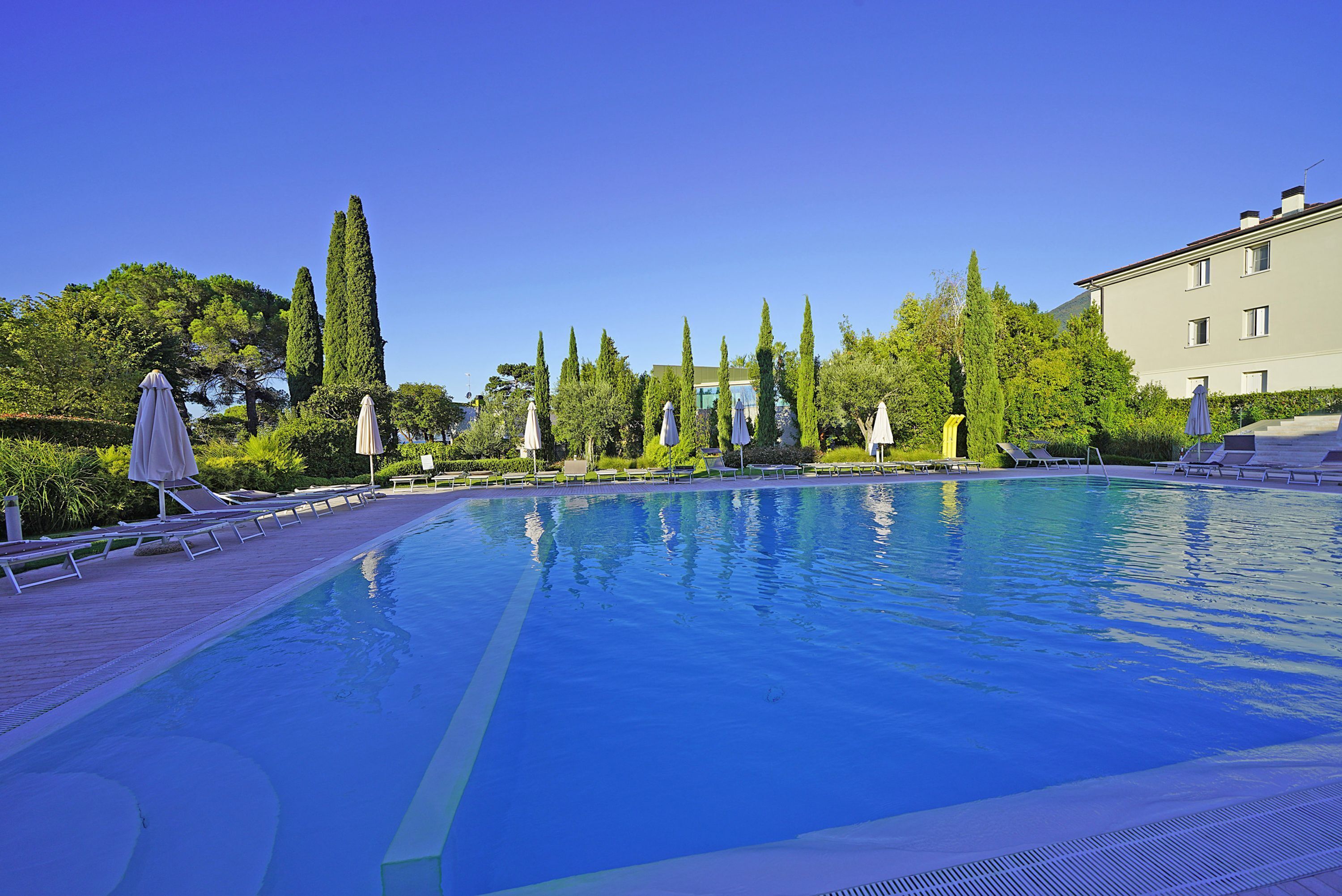 A swimming pool with lounge chairs and umbrellas, surrounded by trees and a building.