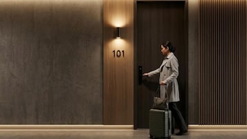 A person entering a room with a wooden door marked '101', a wall-mounted light, and a suitcase.