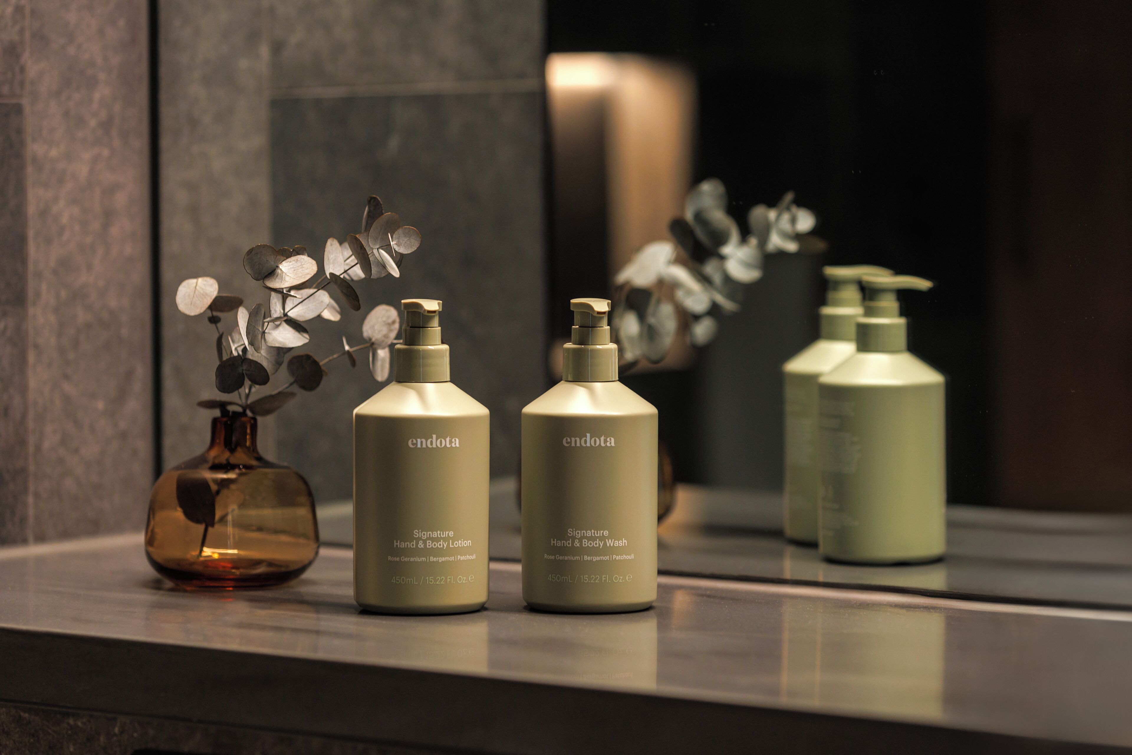 Three bottles of Endota Signature Hand & Body Lotion and Hand & Body Wash on a reflective surface.