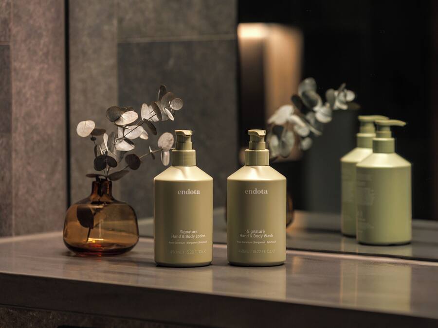 Three bottles of Endota Signature Hand & Body Lotion and Hand & Body Wash on a reflective surface.