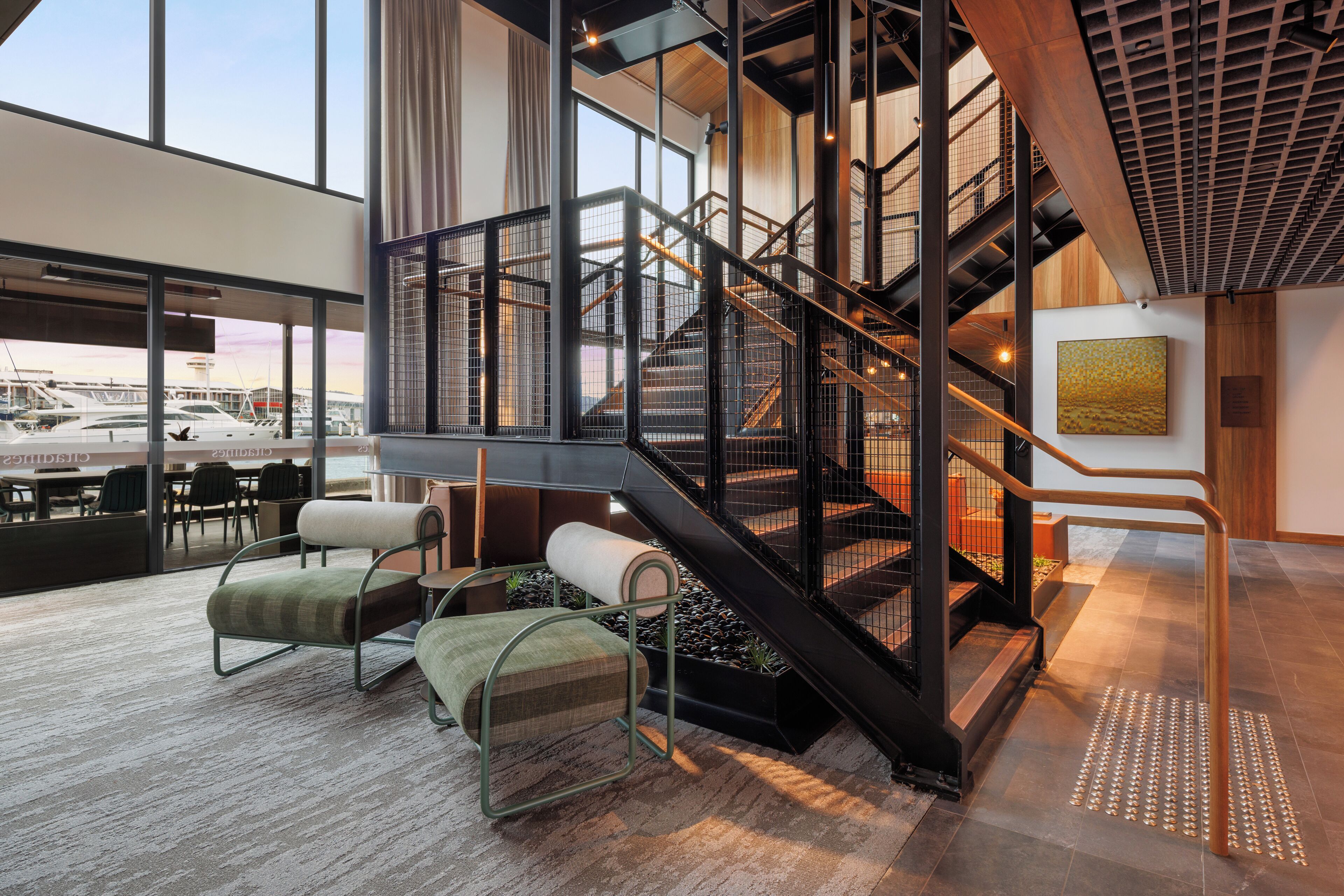 A modern interior with a staircase, seating area, and large windows overlooking a marina.