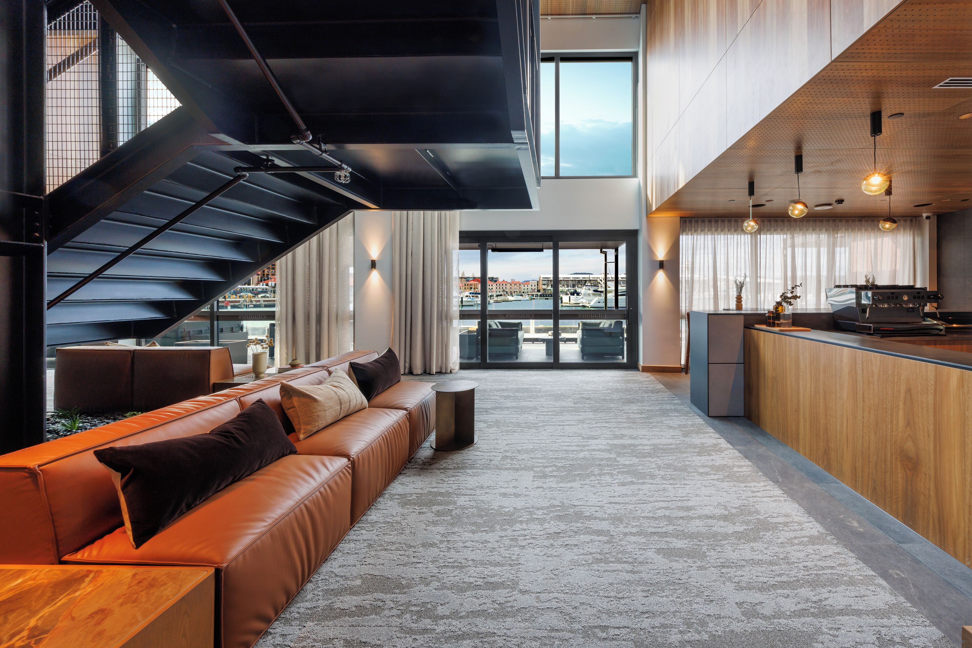 A modern interior with a leather sofa, a kitchen area, and a view of the marina.