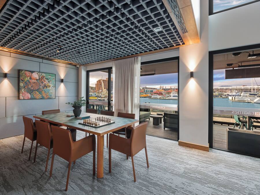 A modern dining area with a chessboard, a large window overlooking a marina, and a cityscape view.