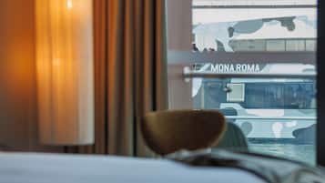 A hotel room with a bed, a lamp, and a window view of a bridge and buildings.