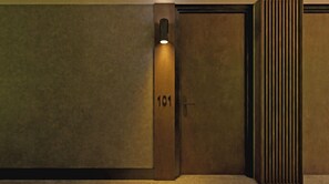 Een kamer met een deur waarop '101' staat, een lamp boven de deur en een structuurwand.