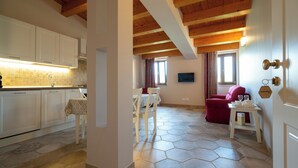 Une cuisine avec des meubles blancs, un coin repas avec une table et des chaises, un canapé rouge et une petite table d’appoint sur laquelle sont posés divers objets.