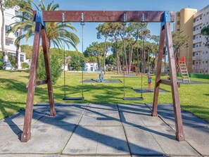 Un parque con columpios, un área de juegos y un edificio al fondo.