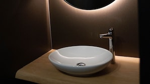 Een badkamer met een ronde spiegel, een witte wastafel en een houten aanrechtblad.