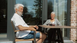 Twee personen zitten aan een tafel voor een gebouw met grote ramen.