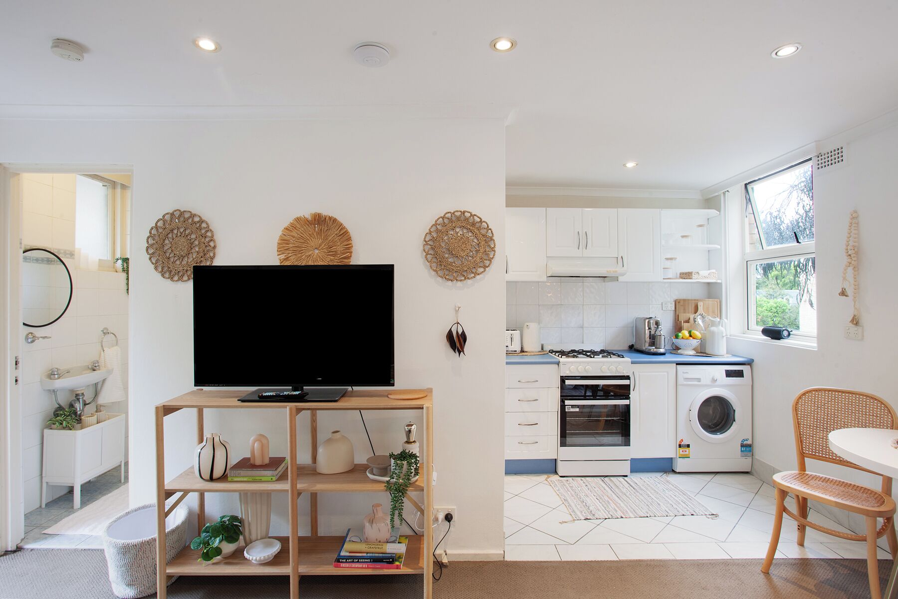 Une cuisine moderne avec des meubles blancs, une cuisinière à gaz, un lave-linge et un coin repas comprenant une chaise et une table.