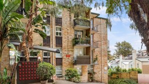 Un edificio residencial de varios pisos con balcones, fachada de ladrillo y vegetación circundante.