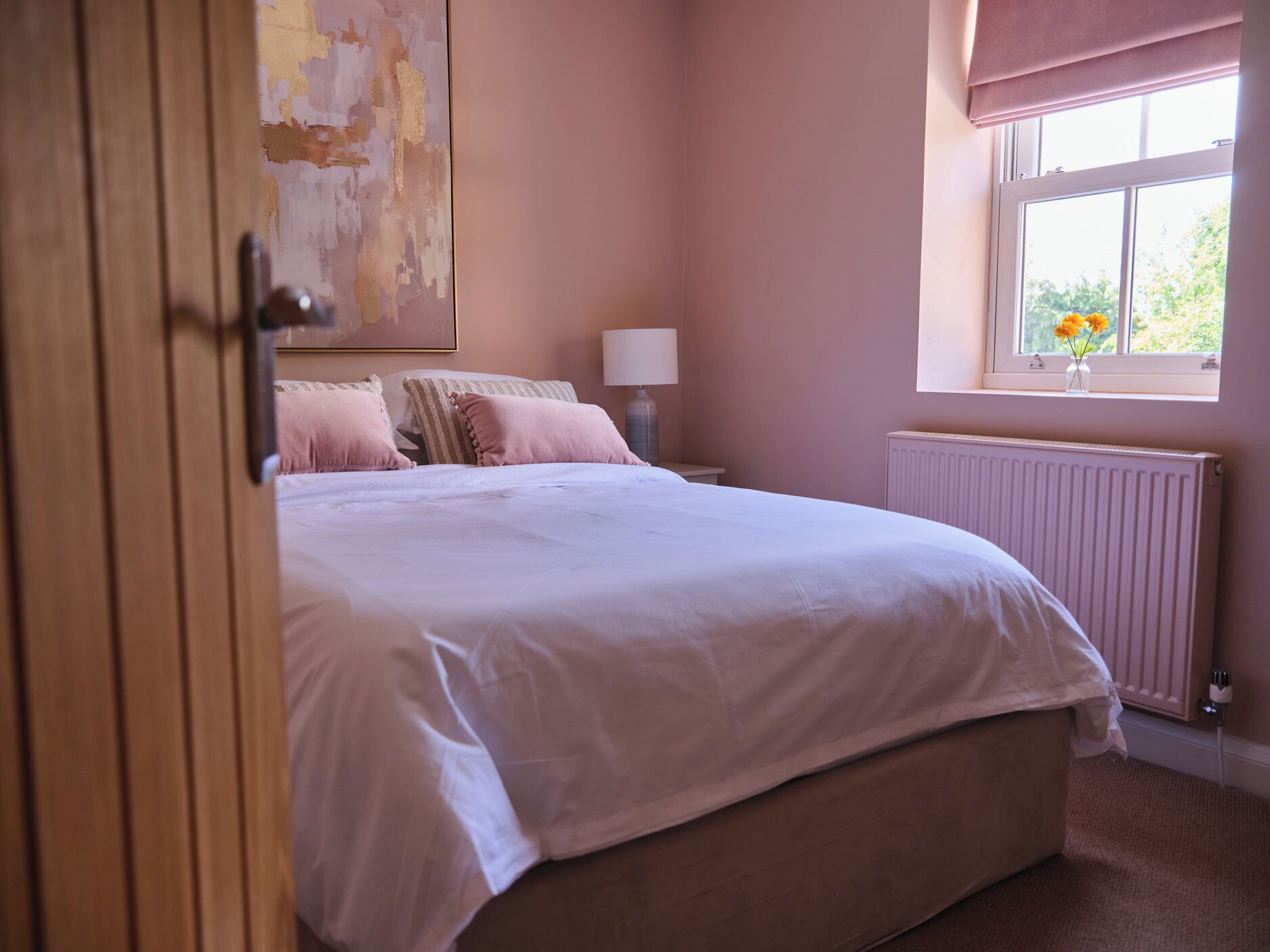 Une chambre à coucher avec un grand lit, une table de chevet, une lampe, un radiateur et une fenêtre décorée de fleurs.