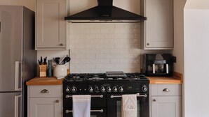 Una cucina con frigorifero in acciaio inossidabile, piano cottura con cappa aspirante nera, macchina da caffè e schienale piastrellato.