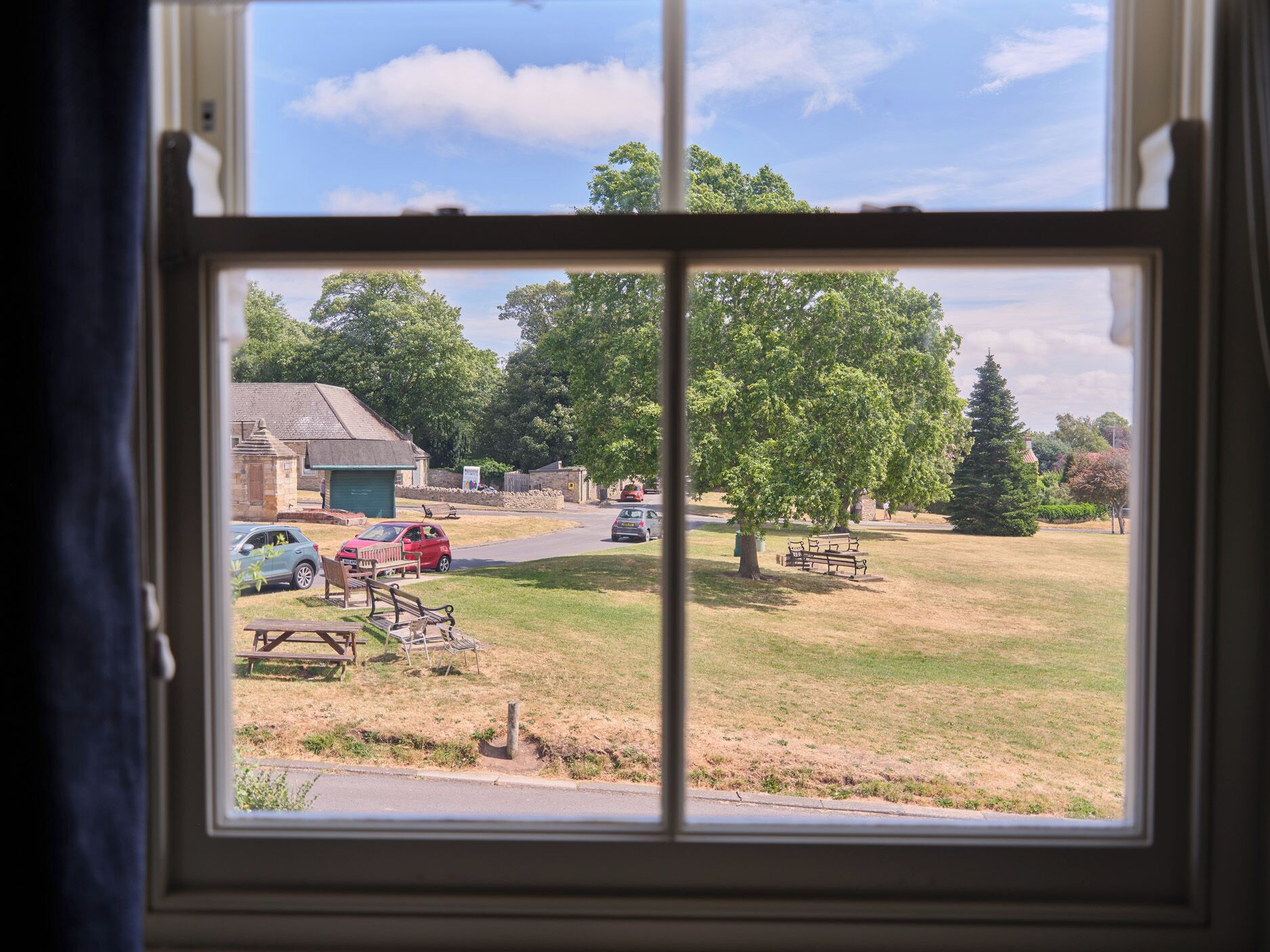 A window view of a grassy area with picnic tables and a car parked nearby.