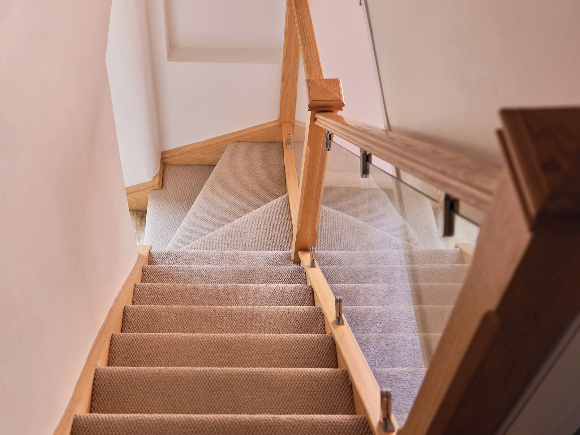 Una escalera alfombrada con barandas de madera y balaustrada de vidrio.