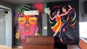 A room with a colorful mural, a brown leather sofa, and a ceiling fan. - Amber Hotel & Restaurant (Hurara)