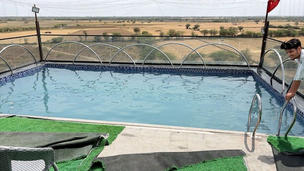 A swimming pool with a view of a rural landscape, a metal railing, and a person standing by the pool. - Amber Hotel & Restaurant (Hurara)
