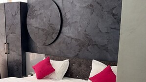 A bed with white bedding and two pink pillows, a dark headboard, and a circular wall decoration. - Amber Hotel & Restaurant (Hurara)