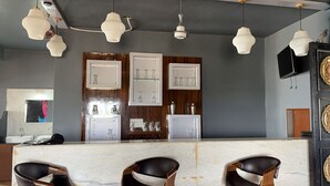 A bar area with a marble countertop, black leather bar stools, hanging pendant lights, and framed glassware on shelves. - Amber Hotel & Restaurant (Hurara)