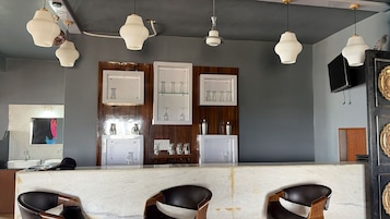 Zona de bar con mostrador de mármol, taburetes de cuero negro, lámparas colgantes y copas en estanterías.