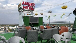 An outdoor seating area with a sign reading 'AMBER HOTEL' and a view of the landscape. - Amber Hotel & Restaurant (Hurara)