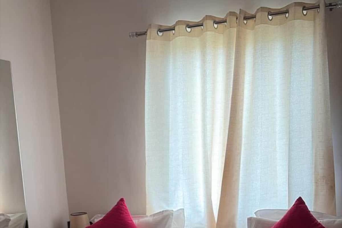 A hotel room with a bed, two pillows, a bedside table, a lamp, and a chair.