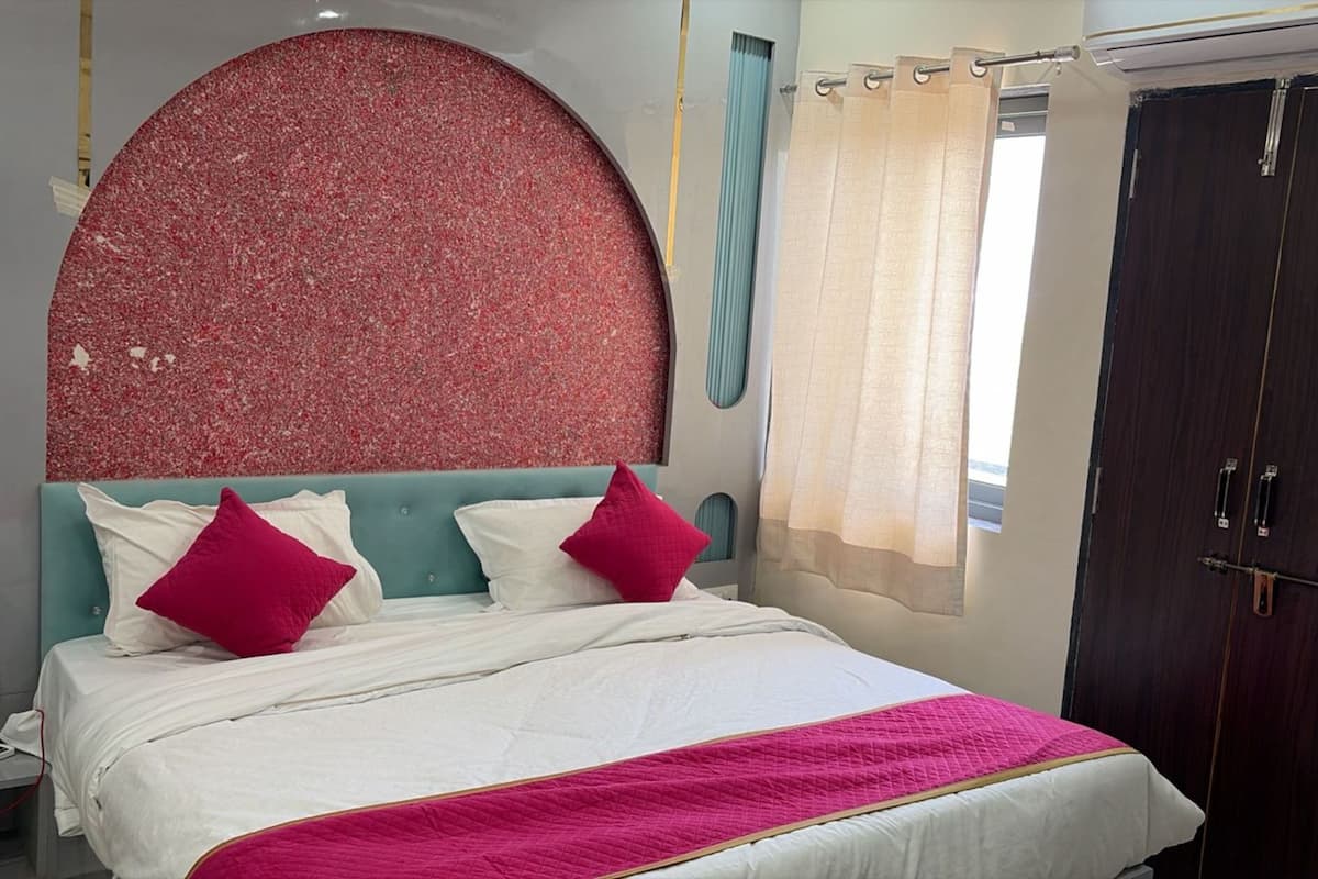 A bed with a white and pink quilt, a red textured headboard, and a dark wooden wardrobe.