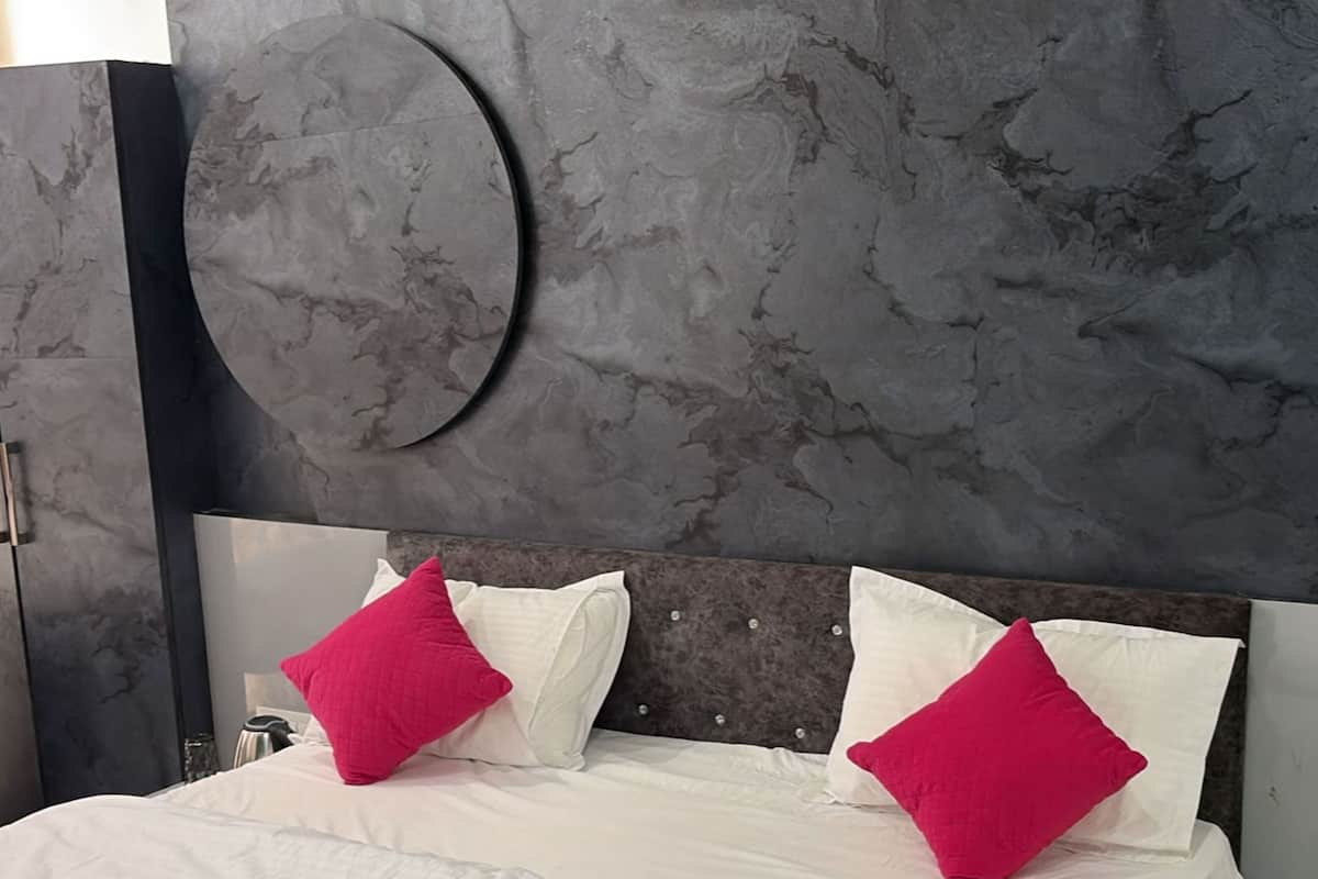 A bed with white bedding and two bright pink pillows, a round wall decoration, and a dark headboard.