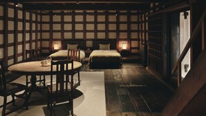 A traditional Japanese-style room with tatami flooring, a low table with chairs, and two beds with pillows and nightstands. - Old Soma Residence Kazeno Heritage (Hakodate)