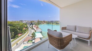 Ein Balkon mit Blick auf einen Pool und Gebäude, ein Korbstuhl und eine Couch.