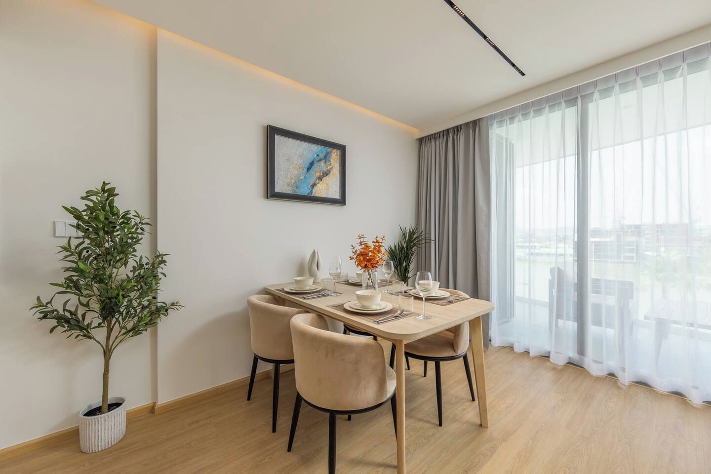 A dining area with a table set for four, a potted plant, and a framed picture on the wall.