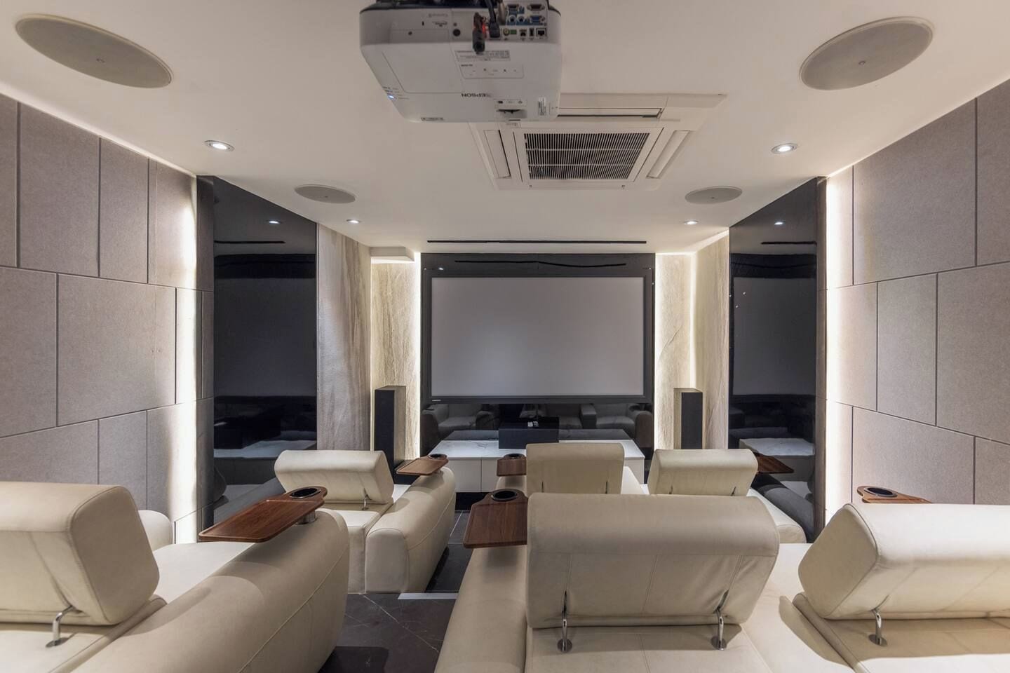A modern home theater with a large screen, comfortable seating, and a ceiling-mounted projector.