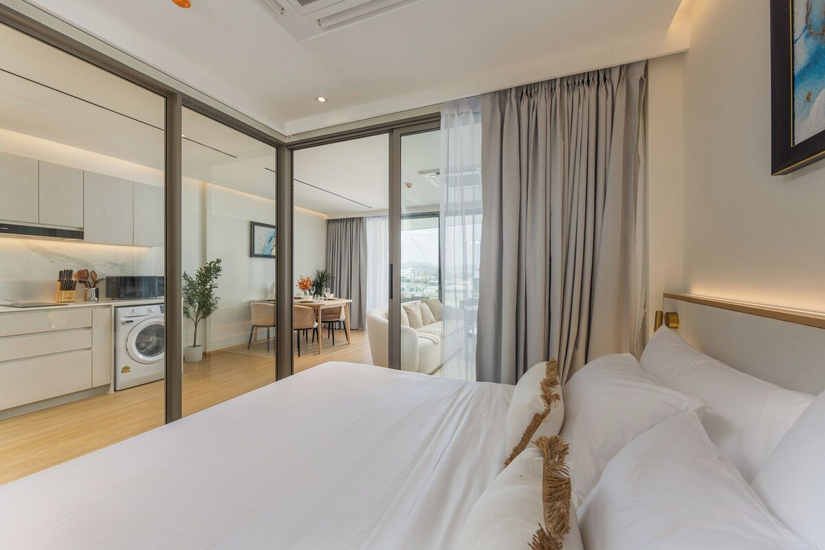 Ein modernes Hotelzimmer mit einem großen Bett, einem Essbereich und Blick durch eine Glastür.