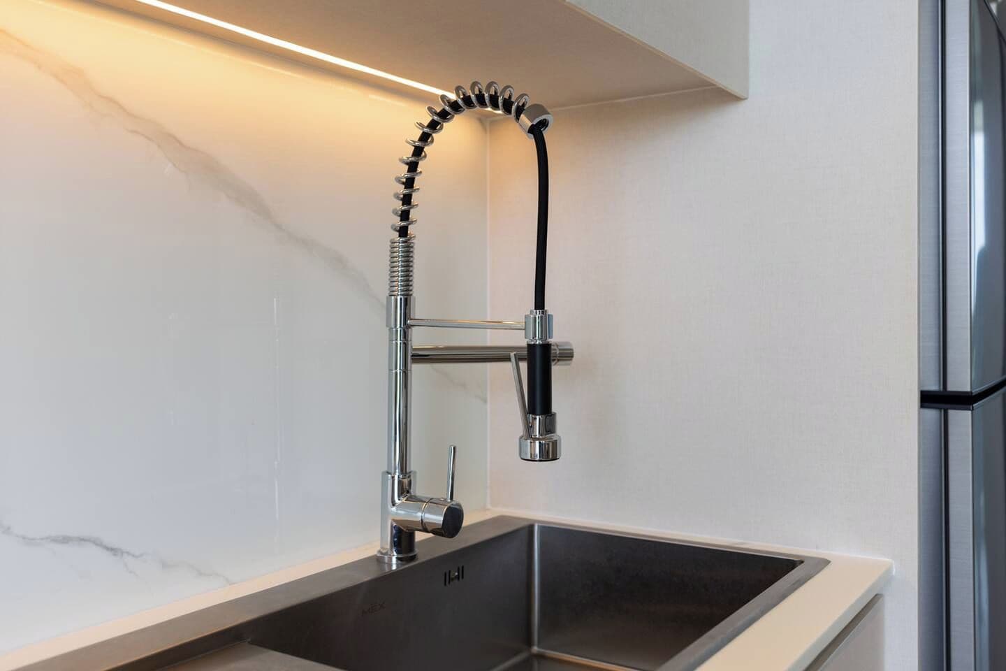 A modern kitchen with a stainless steel faucet, a black hose, and a marble countertop.