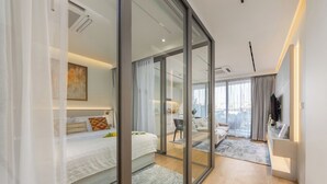 Ein modernes Hotelzimmer mit einem großen Bett, einem Schreibtisch, einer Sitzecke und Blick durch eine Glastür.