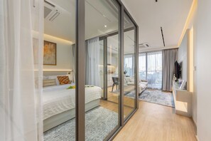 Ein modernes Hotelzimmer mit einem großen Bett, einem Schreibtisch, einer Sitzecke und Blick durch eine Glastür.