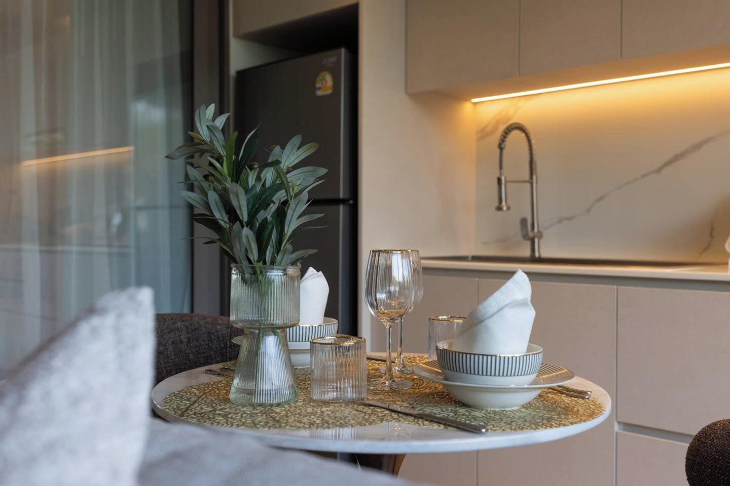 A dining table with a vase of green plants, wine glasses, and a bowl with a napkin.