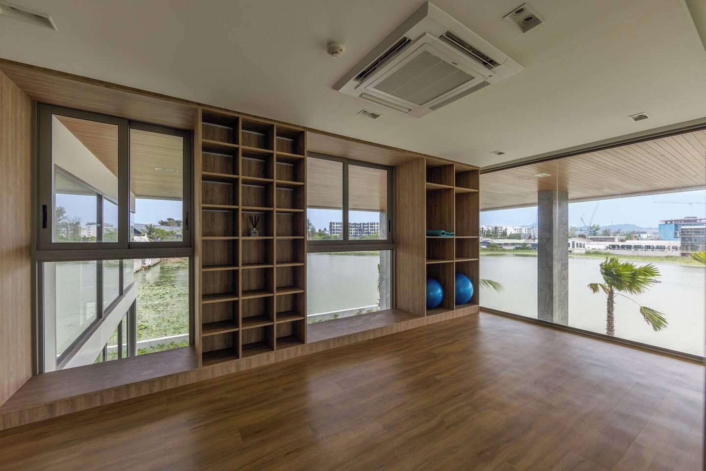 A spacious room with large windows, a wooden floor, and a built-in shelving unit.