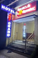 Entrada de un hotel con un letrero de neón que dice 'HOTEL GRAND' y otro letrero que dice 'JP'.
